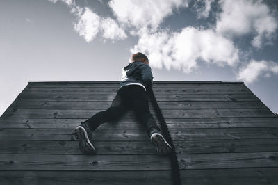 Low angle view of boy sitting on wood against sky