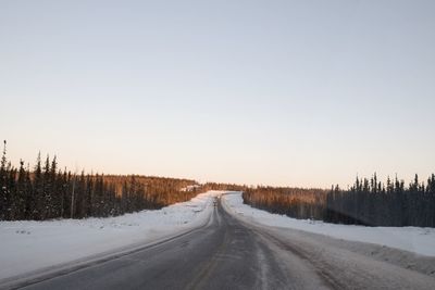 Road amidst trees against clear sky during winter