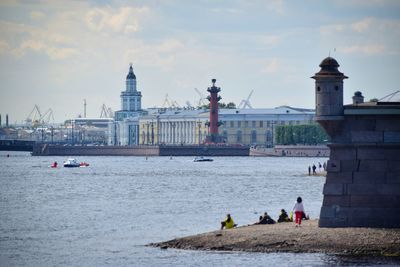 People at waterfront against cloudy sky