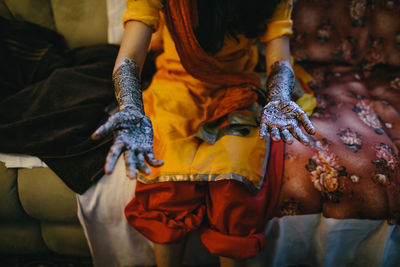 Midsection of woman with henna tattoo on hand sitting at home