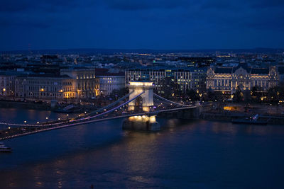 Illuminated bridge over river in city at night