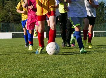 Low section of teenage boys playing soccer on field