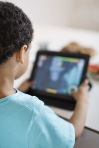 Rear view of boy playing game on digital tablet at home