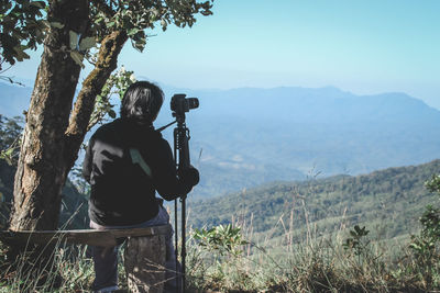 Rear view of man photographing mountains against sky