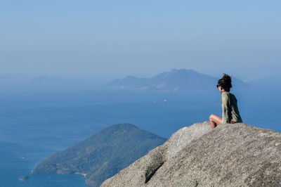 Man sitting on rock looking at mountains against sky