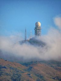 Weather radar station by mountain against sky