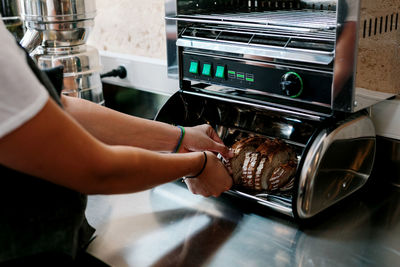 From above crop cook putting fresh rye bread into metal toaster while preparing food in cafe