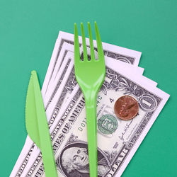 High angle view of currency and plastic cutlery on green background