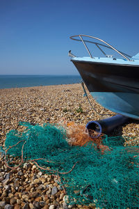 Turquoise and orange fishing net on a shingle beach next to a fishing boat with clear blue sky