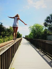 Rear view of woman balancing on boardwalk railing