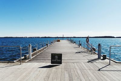 Warning sign on pier amidst river against clear sky on sunny day