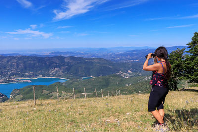 Woman looking through binoculars while standing on land