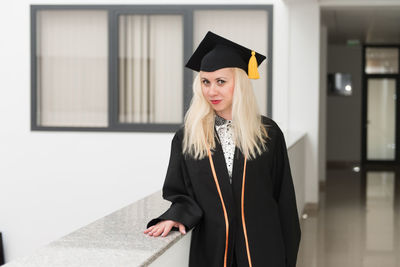 Portrait of smiling young woman wearing graduation gown standing in city