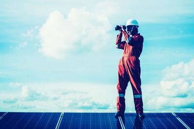 Low angle view of male technician inspecting solar panels against sky