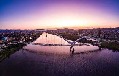 Bridge over river amidst buildings against sky during sunset