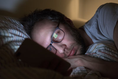 Sleepy male with glasses surfing in web before sleeping. social media addict, sleeplessness concept.