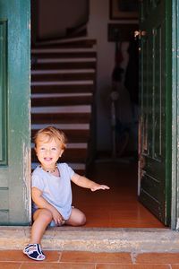 Full length of cute boy sitting at door of house