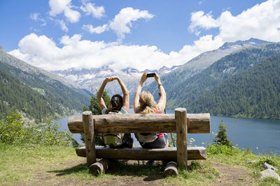 Rear view of people sitting on bench against mountains