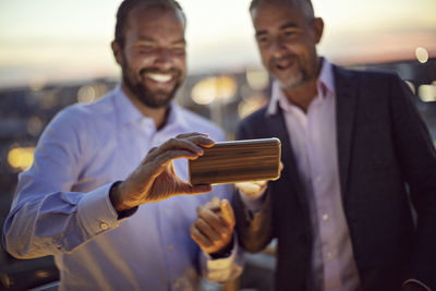 Businessmen taking selfie on smart phone at terrace during sunset