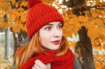 Smiling cute young woman in orange warm knitted hat and scarf. autumn portrait close-up.