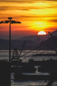 Silhouette crane by sea against orange sky