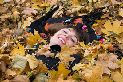 Portrait of smiling mid adult woman lying on autumn leaves at park