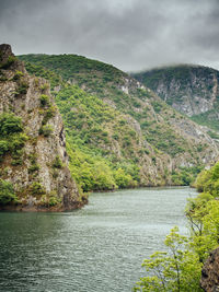 Scenic view of river by tree mountains against sky