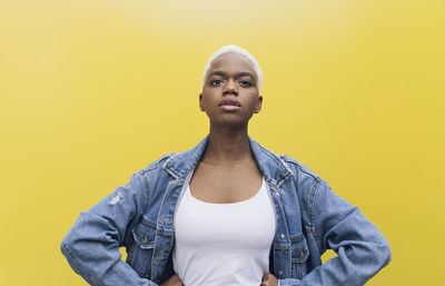 Confident woman with hands on hips standing against yellow background