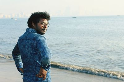 Portrait of young man standing at beach against sky