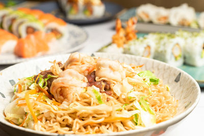 Delicious noodles with prawns, barbecued pork, carrots in the background several sushi dishes.