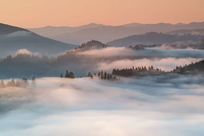 Scenic view of fog covered mountains against sky during sunrise