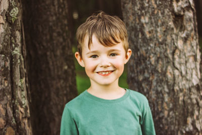 Portrait of cute boy looking away standing against tree trunk