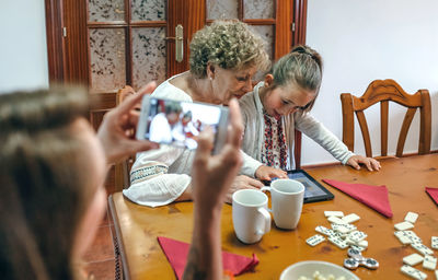 Woman photographing family playing mobile game at table