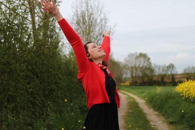 Smiling woman standing with arms raised against plants