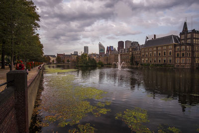 View of buildings by river against cloudy sky