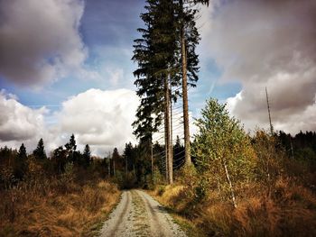 Road passing through field against cloudy sky