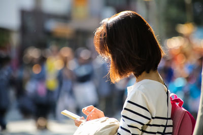 Rear view of woman using mobile phone in city