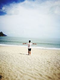Rear view of man with arms outstretched standing on beach against sky