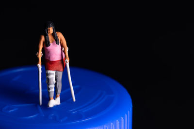 A young woman with a broken leg standing with crutches on a blue medicine bottle