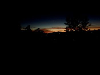 Silhouette trees against clear sky at sunset