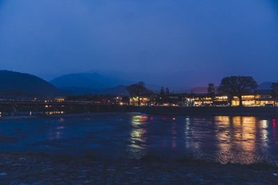 Illuminated city by mountain against sky at dusk