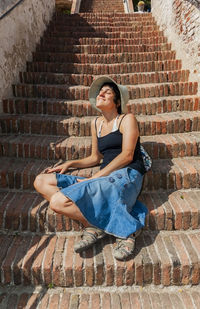 Young woman sitting on staircase against wall