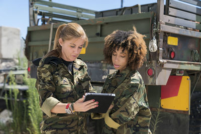 Female military soldiers discussing over digital tablet against truck on sunny day