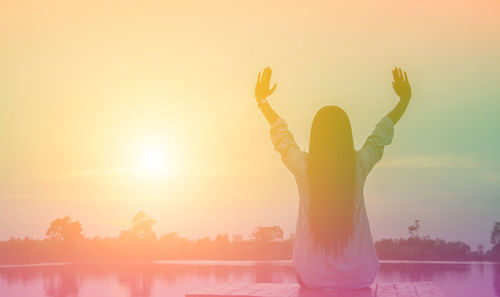 Woman standing by lake against sky during sunset