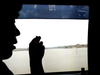 Silhouette woman hand by sea against sky seen through window