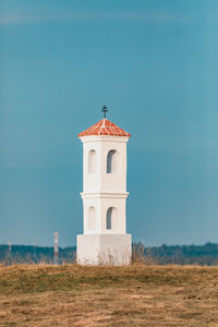 Lighthouse on field by building against sky