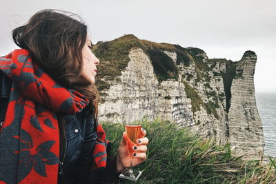 Young woman holding drink against cliff