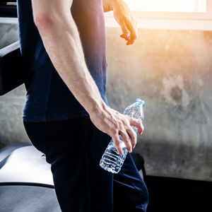 Midsection of man holding water bottle while standing in gym