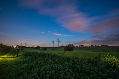 Man with tripod standing on field against sky