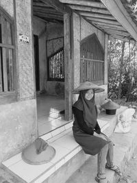 Portrait of a girl in a traditional indonesian bamboo farmer hat sits in front of an old house